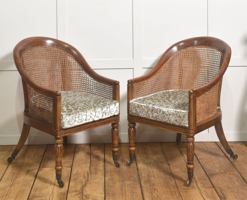 Pair of Regency style mahogany tub chairs featuring woven cane backs, upholstered cushions, turned legs, and brass castors.