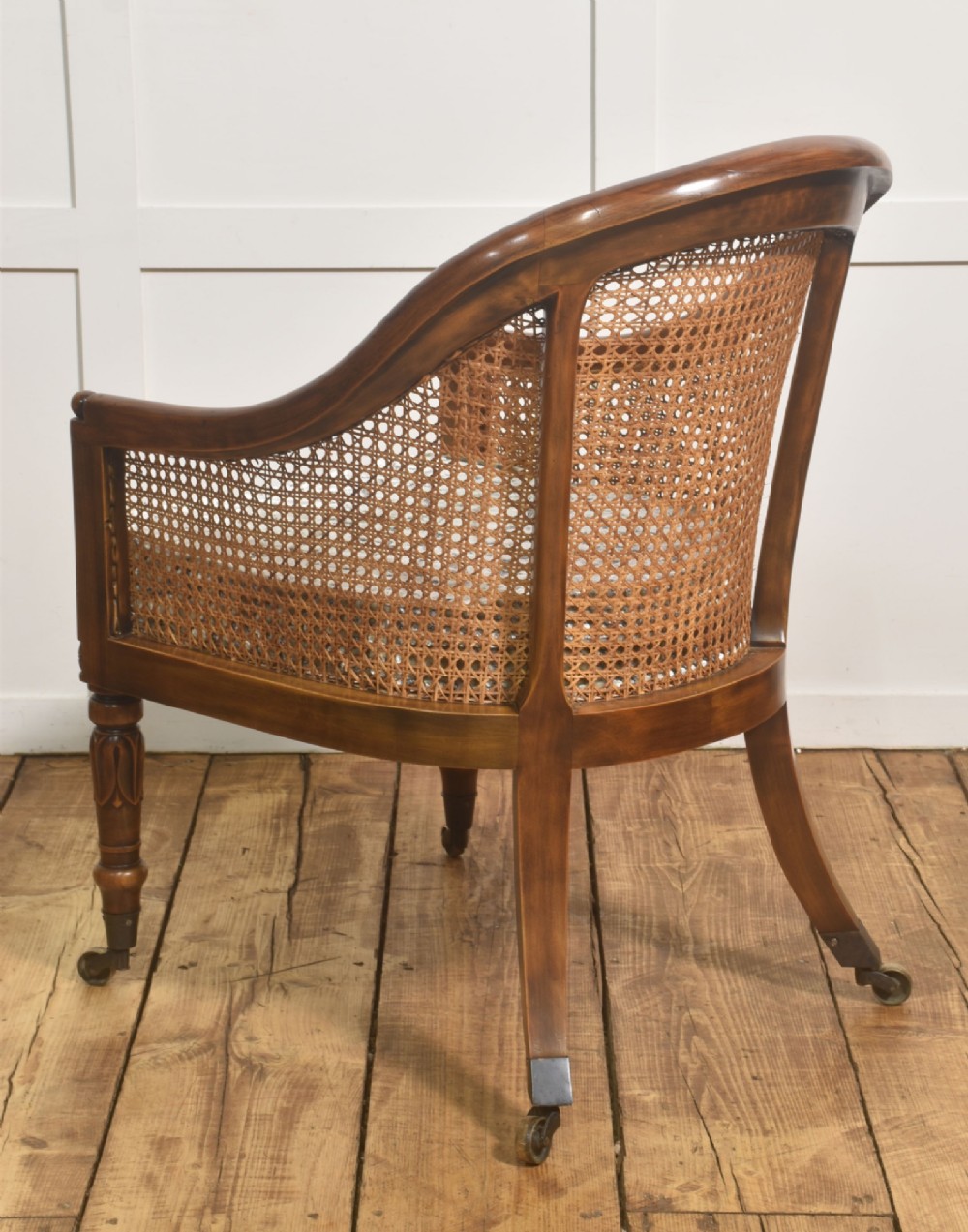 Pair of Regency style mahogany tub chairs featuring woven cane backs, upholstered cushions, turned legs, and brass castors. View X