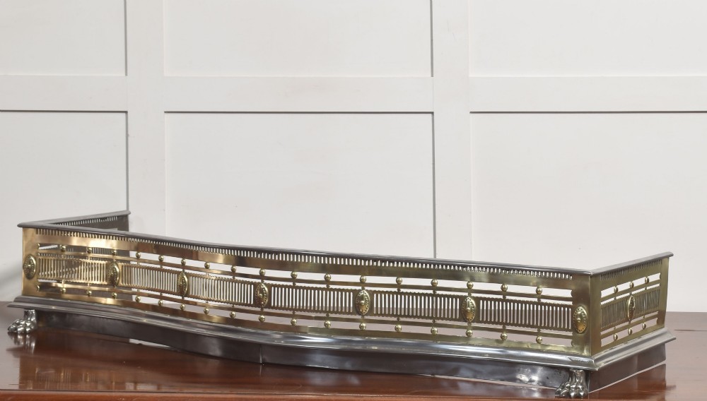 A 19th-century Regency fire fender featuring a pierced brass gallery with oval central bosses, mounted on a polished steel base with claw feet. View II