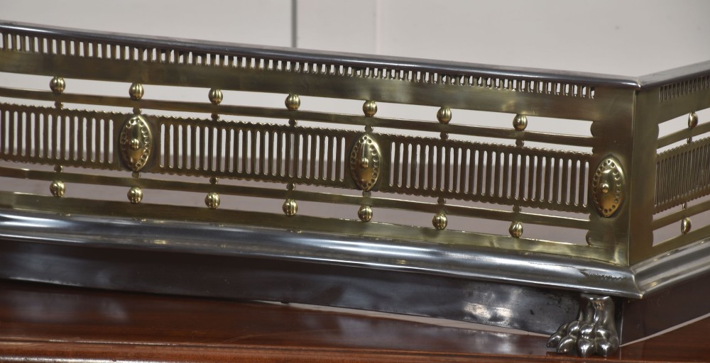 A 19th-century Regency fire fender featuring a pierced brass gallery with oval central bosses, mounted on a polished steel base with claw feet. View III