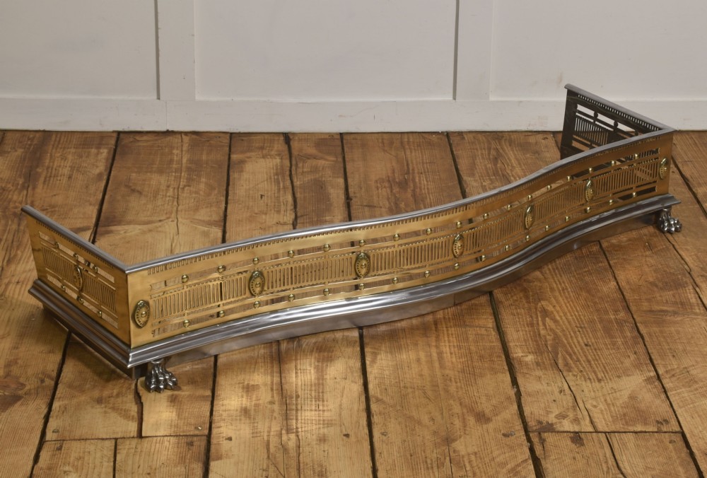 A 19th-century Regency fire fender featuring a pierced brass gallery with oval central bosses, mounted on a polished steel base with claw feet. View IV