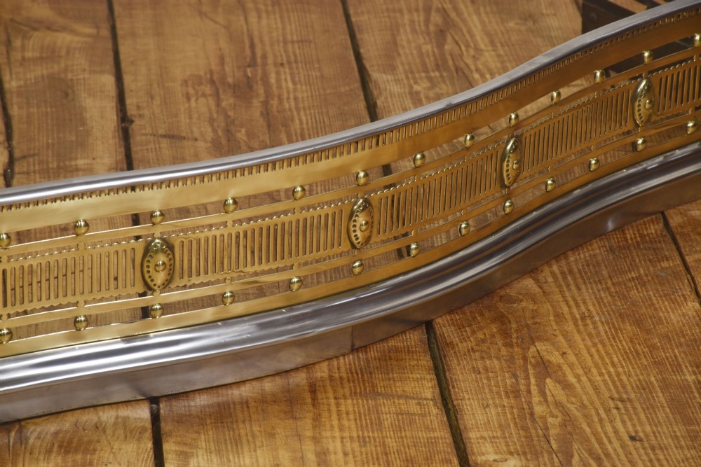 A 19th-century Regency fire fender featuring a pierced brass gallery with oval central bosses, mounted on a polished steel base with claw feet. View V