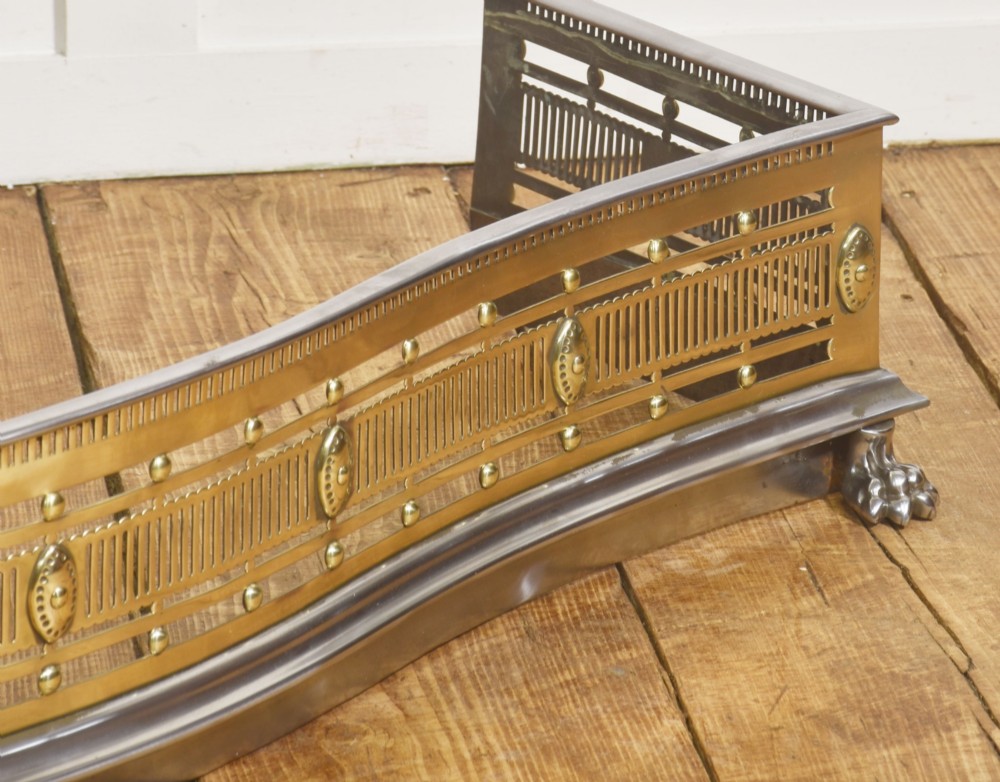 A 19th-century Regency fire fender featuring a pierced brass gallery with oval central bosses, mounted on a polished steel base with claw feet. View VI