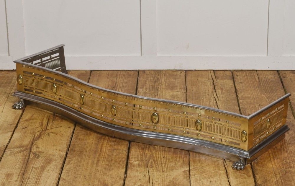 A 19th-century Regency fire fender featuring a pierced brass gallery with oval central bosses, mounted on a polished steel base with claw feet. View VII