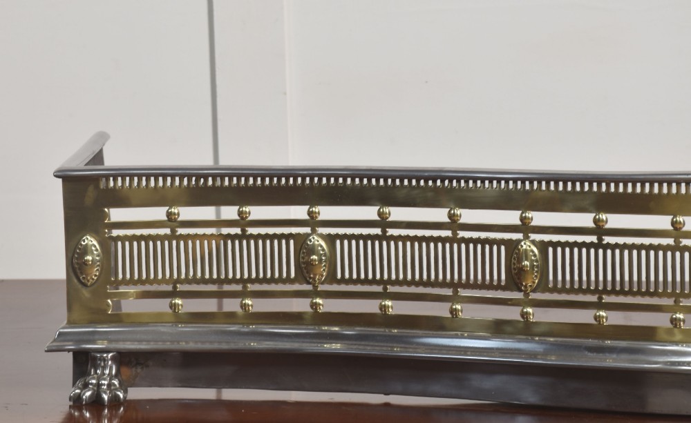 A 19th-century Regency fire fender featuring a pierced brass gallery with oval central bosses, mounted on a polished steel base with claw feet. View VIII