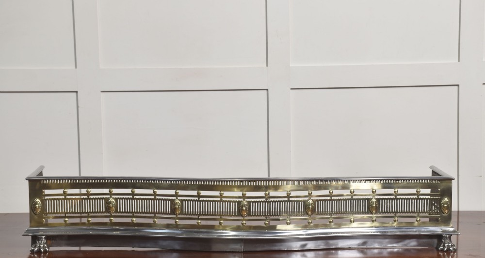 A 19th-century Regency fire fender featuring a pierced brass gallery with oval central bosses, mounted on a polished steel base with claw feet. View X