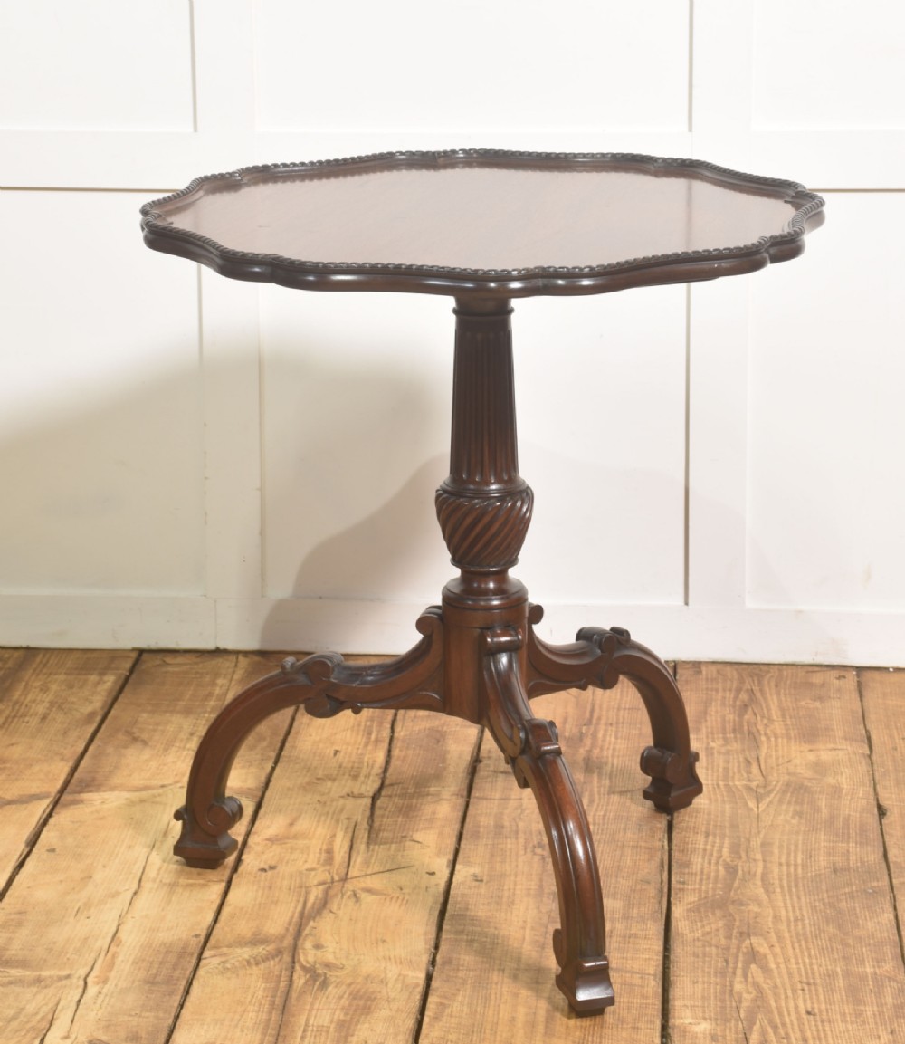 A dark carved mahogany tripod occasional table featuring a scalloped piecrust top, fluted central pedestal, and carved cabriole legs.