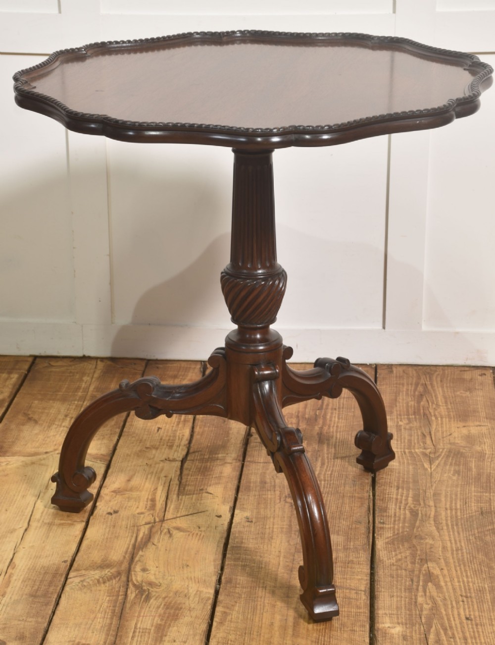 A dark carved mahogany tripod occasional table featuring a scalloped piecrust top, fluted central pedestal, and carved cabriole legs. View VI