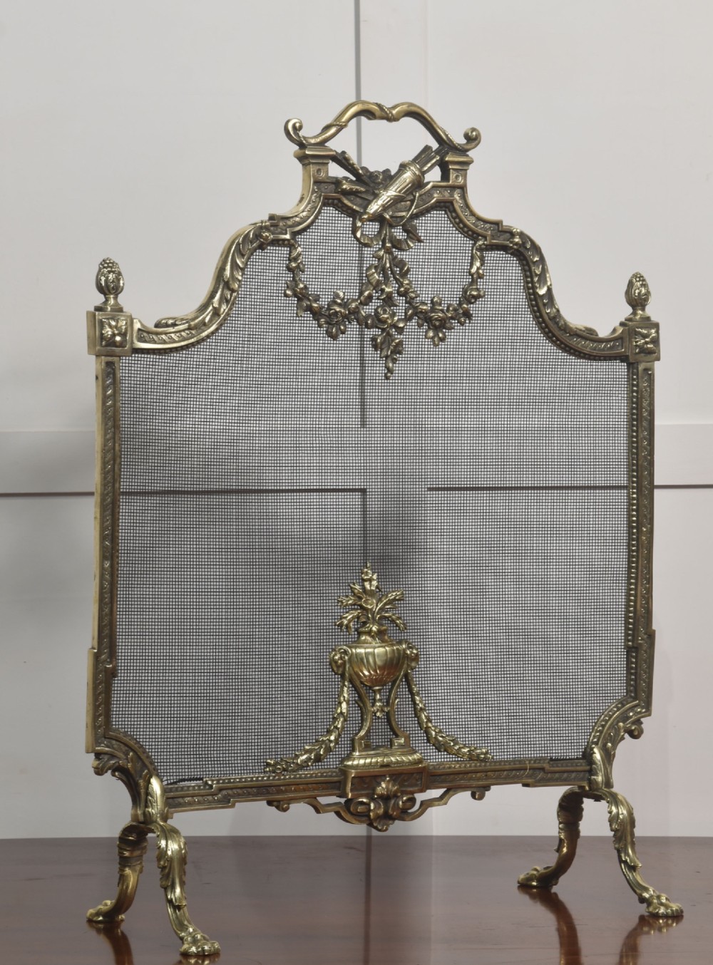 An ornate late 19th-century French gilt brass fire screen featuring a wire mesh panel decorated with a central urn motif, floral swags, and a top crest with a quiver and torch.