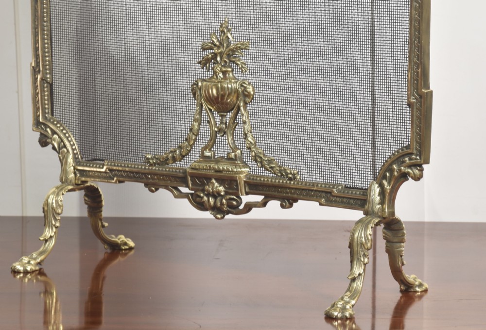 An ornate late 19th-century French gilt brass fire screen featuring a wire mesh panel decorated with a central urn motif, floral swags, and a top crest with a quiver and torch. View IV