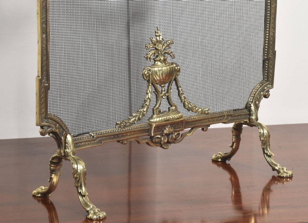 An ornate late 19th-century French gilt brass fire screen featuring a wire mesh panel decorated with a central urn motif, floral swags, and a top crest with a quiver and torch. View V