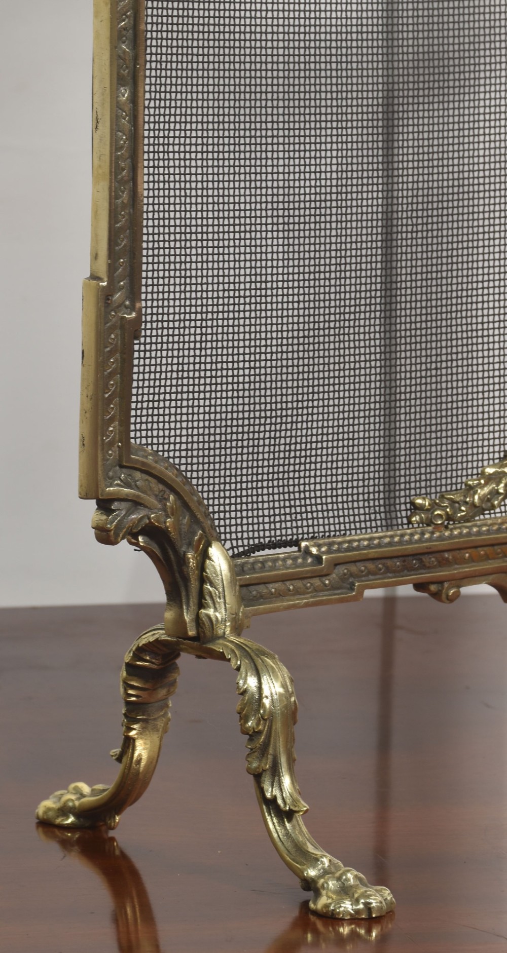 An ornate late 19th-century French gilt brass fire screen featuring a wire mesh panel decorated with a central urn motif, floral swags, and a top crest with a quiver and torch. View VI