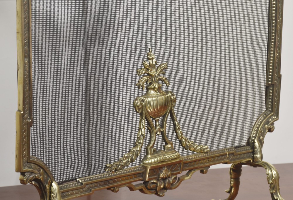 An ornate late 19th-century French gilt brass fire screen featuring a wire mesh panel decorated with a central urn motif, floral swags, and a top crest with a quiver and torch. View VIII