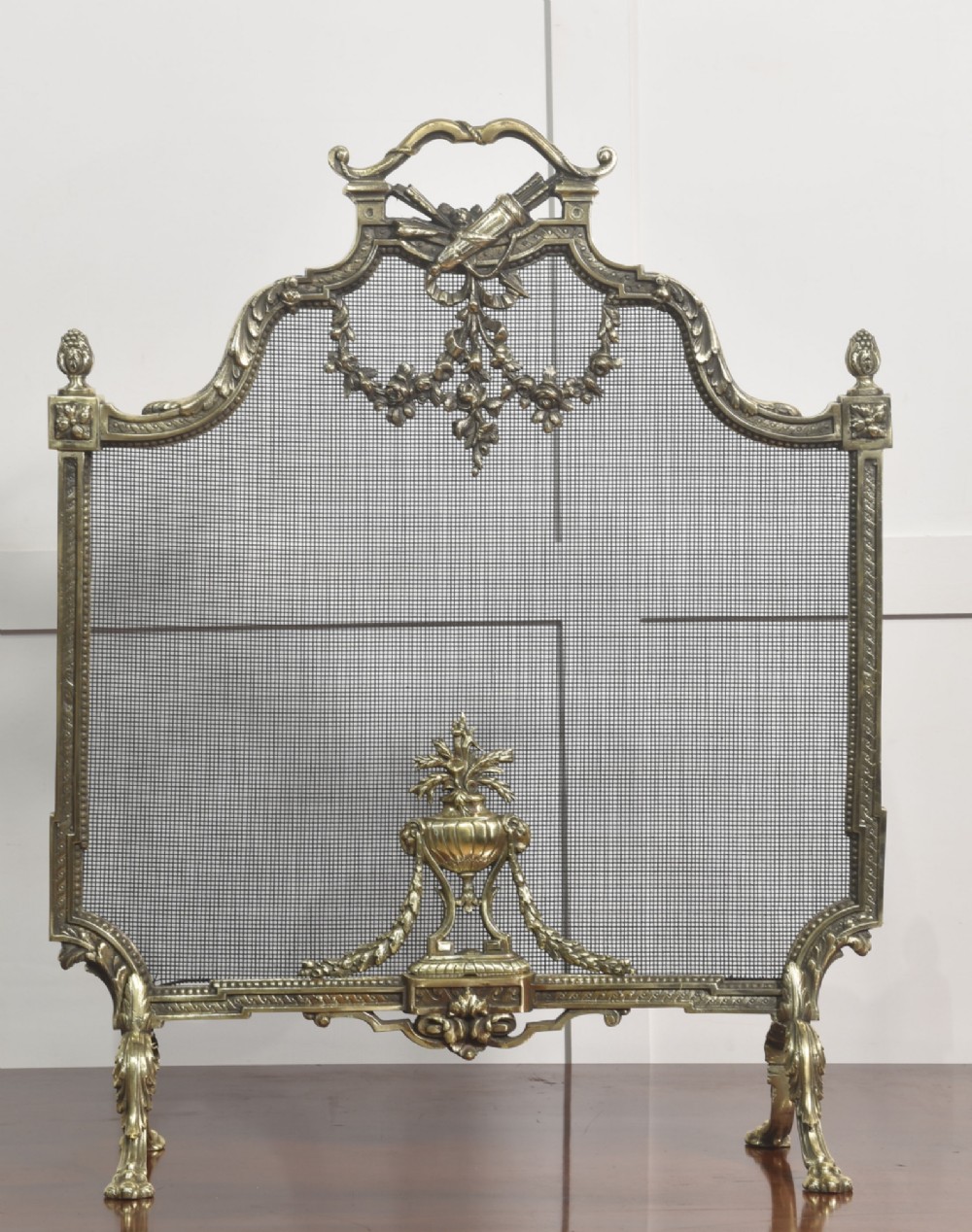 An ornate late 19th-century French gilt brass fire screen featuring a wire mesh panel decorated with a central urn motif, floral swags, and a top crest with a quiver and torch. View IX