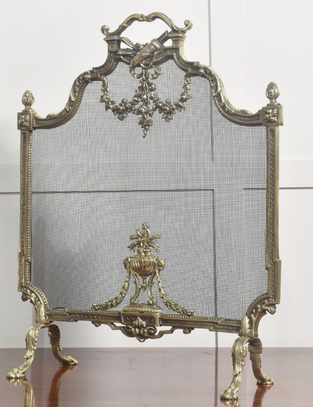 An ornate late 19th-century French gilt brass fire screen featuring a wire mesh panel decorated with a central urn motif, floral swags, and a top crest with a quiver and torch. View X