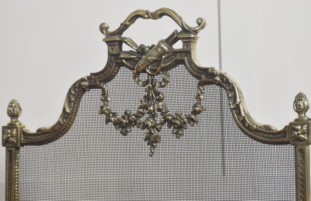 An ornate late 19th-century French gilt brass fire screen featuring a wire mesh panel decorated with a central urn motif, floral swags, and a top crest with a quiver and torch. View XI
