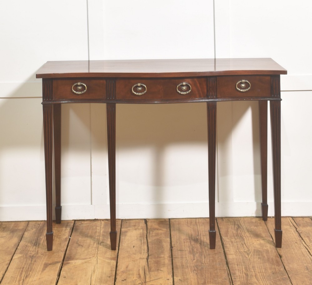 An Edwardian mahogany bow-fronted side table featuring four drawers with brass ring handles and slender fluted legs ending in spade feet.