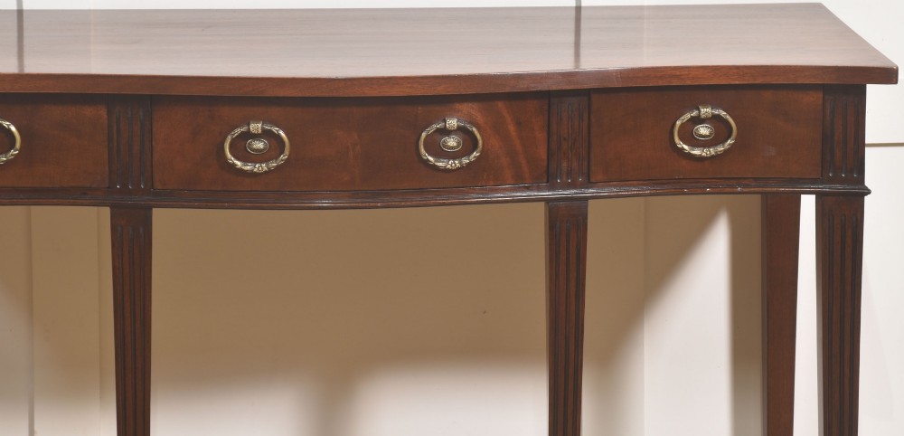 An Edwardian mahogany bow-fronted side table featuring four drawers with brass ring handles and slender fluted legs ending in spade feet. View III