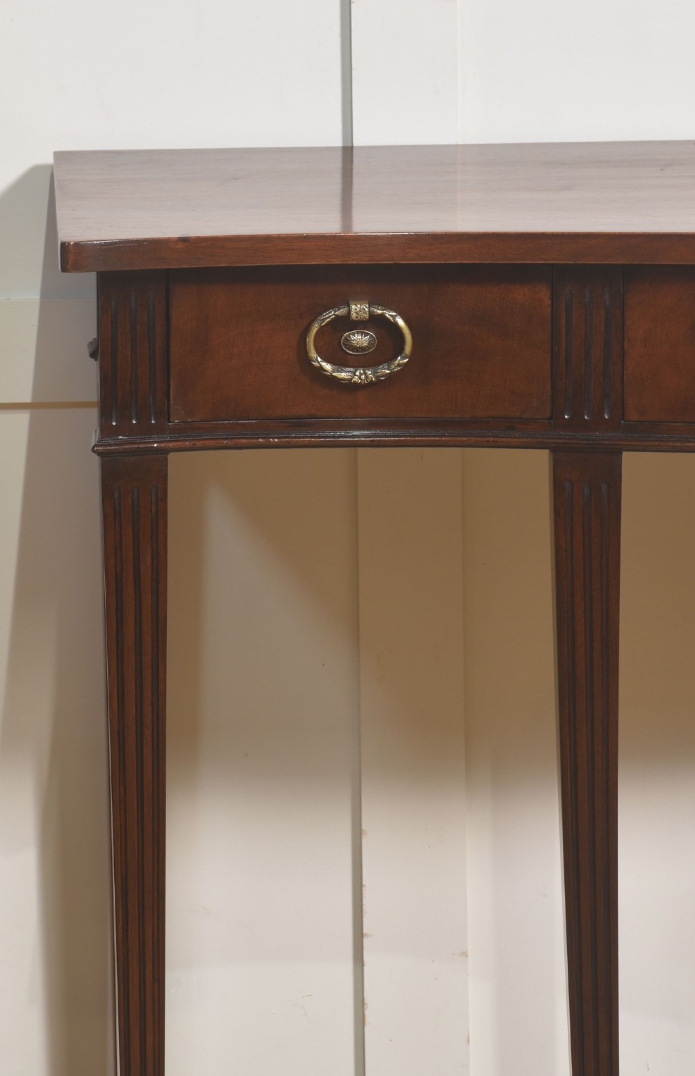 An Edwardian mahogany bow-fronted side table featuring four drawers with brass ring handles and slender fluted legs ending in spade feet. View IV