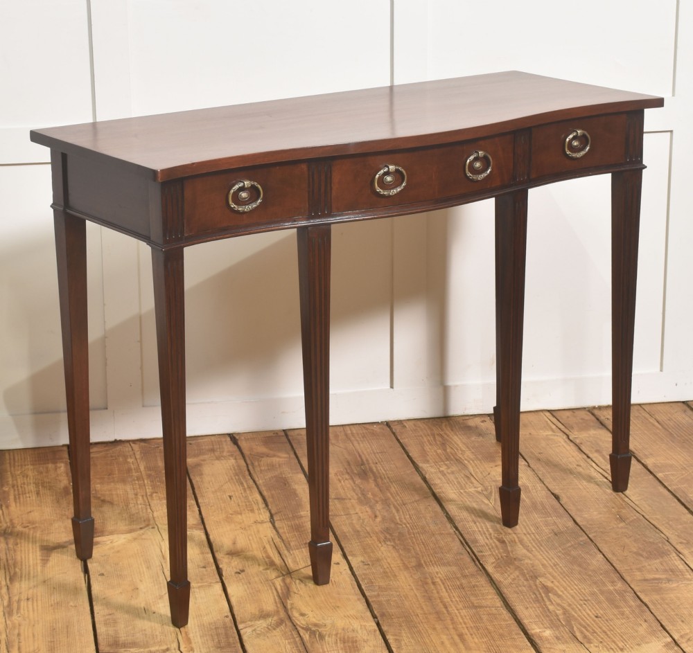 An Edwardian mahogany bow-fronted side table featuring four drawers with brass ring handles and slender fluted legs ending in spade feet. View V