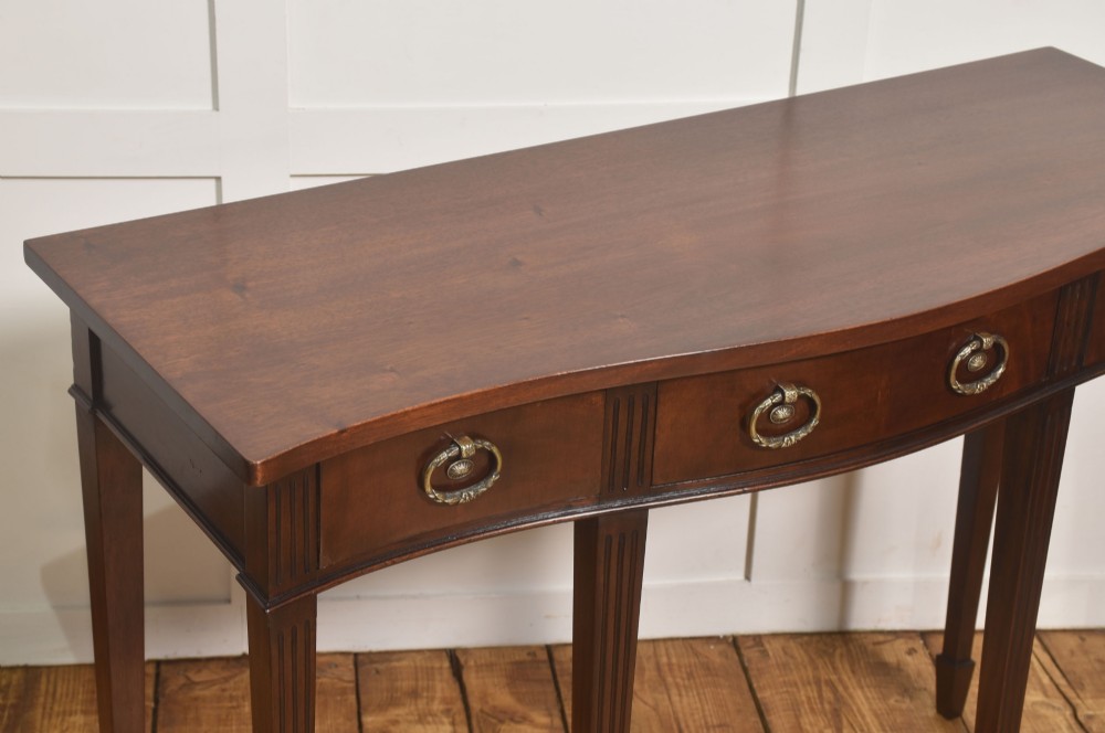 An Edwardian mahogany bow-fronted side table featuring four drawers with brass ring handles and slender fluted legs ending in spade feet. View VI
