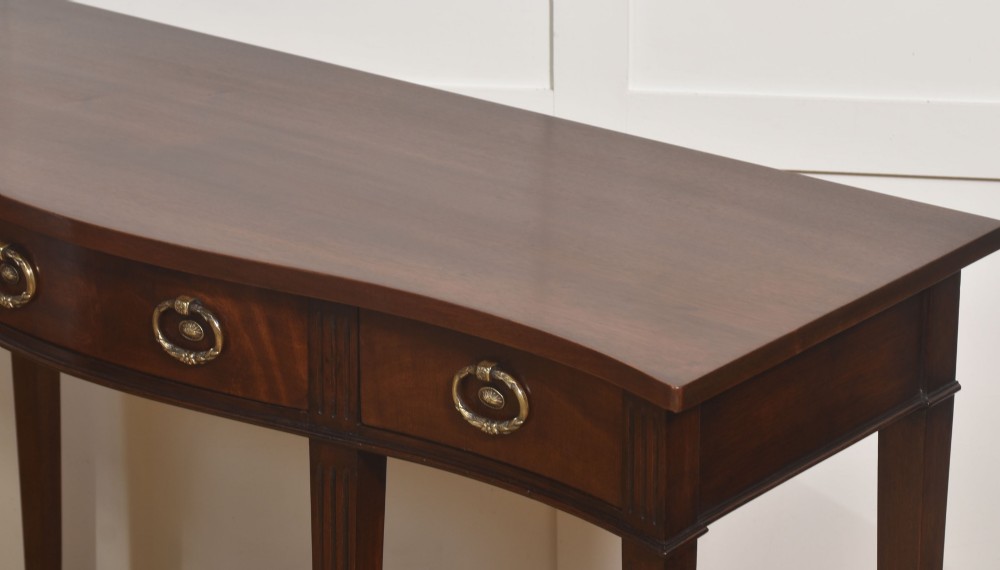 An Edwardian mahogany bow-fronted side table featuring four drawers with brass ring handles and slender fluted legs ending in spade feet. View VII