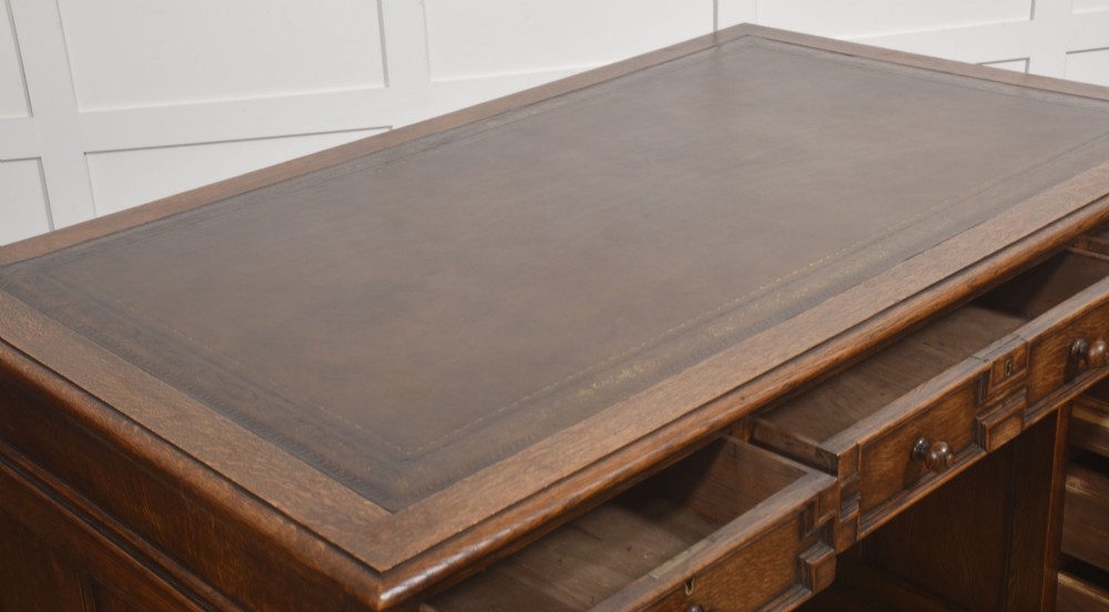 A double-pedestal antique oak partners desk featuring geometric drawer mouldings and an inset brown leather writing top. View II