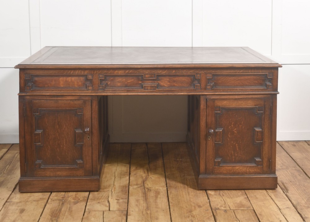 A double-pedestal antique oak partners desk featuring geometric drawer mouldings and an inset brown leather writing top. View VII