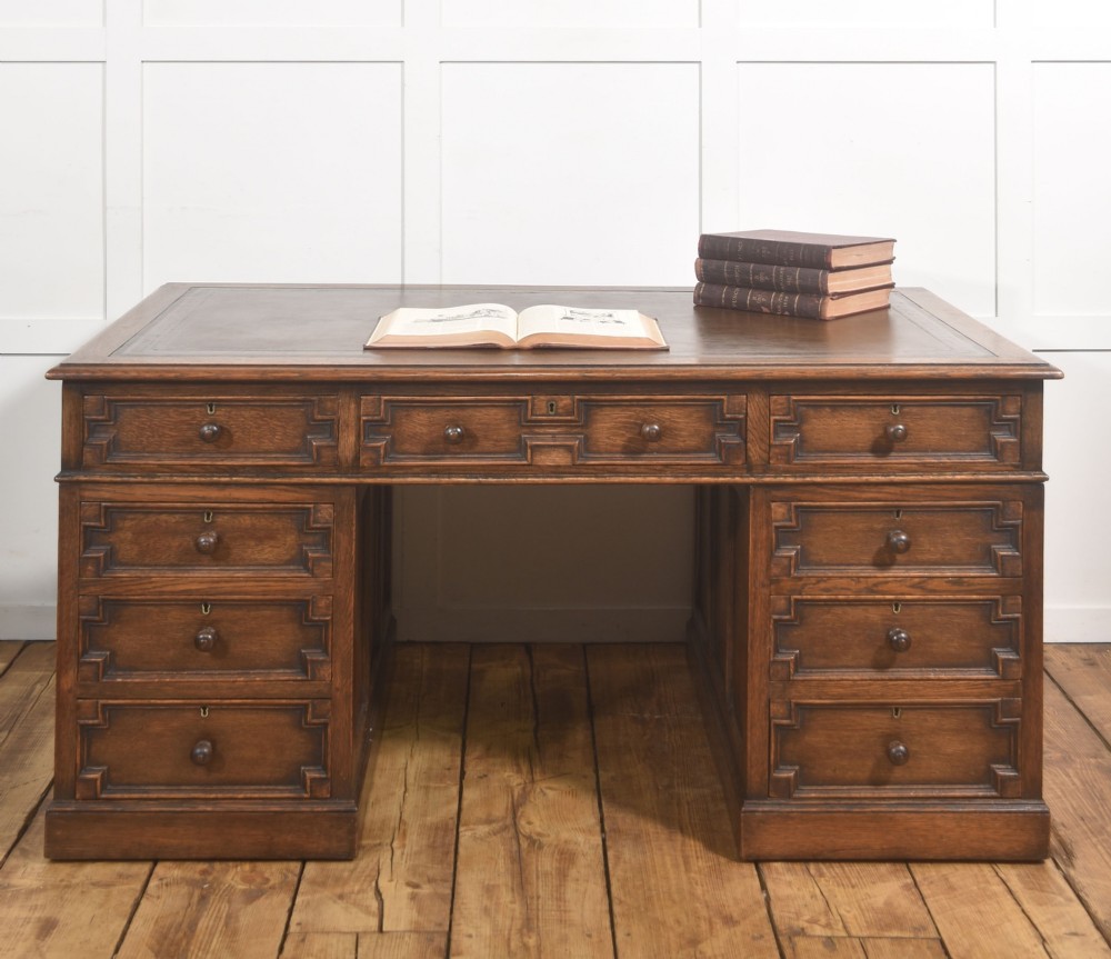 A double-pedestal antique oak partners desk featuring geometric drawer mouldings and an inset brown leather writing top. View IX