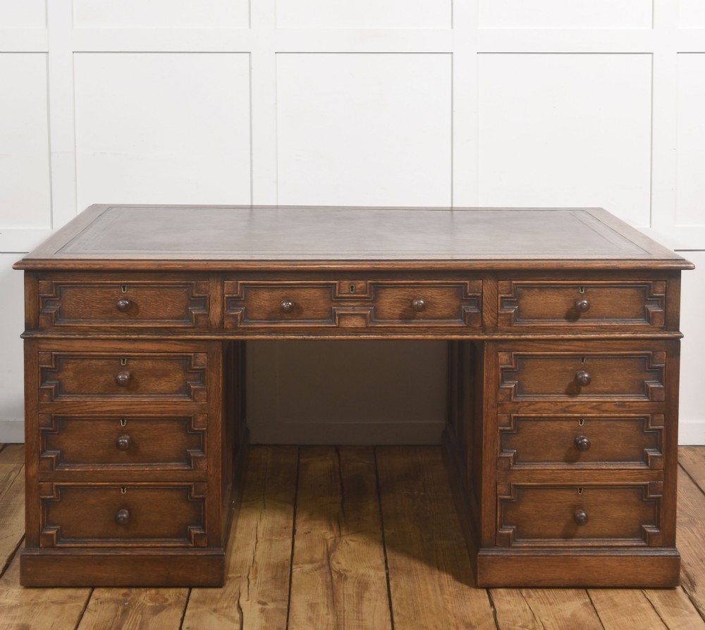 A double-pedestal antique oak partners desk featuring geometric drawer mouldings and an inset brown leather writing top.