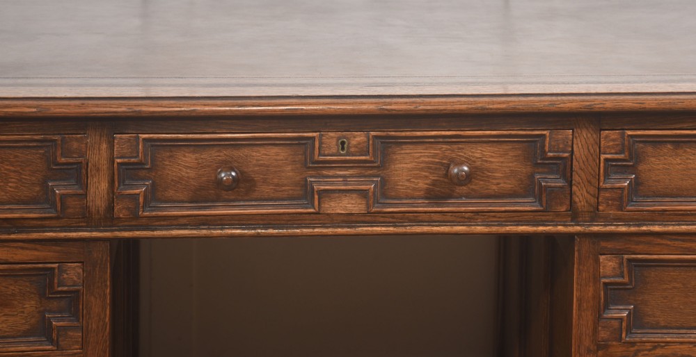 A double-pedestal antique oak partners desk featuring geometric drawer mouldings and an inset brown leather writing top. View XI