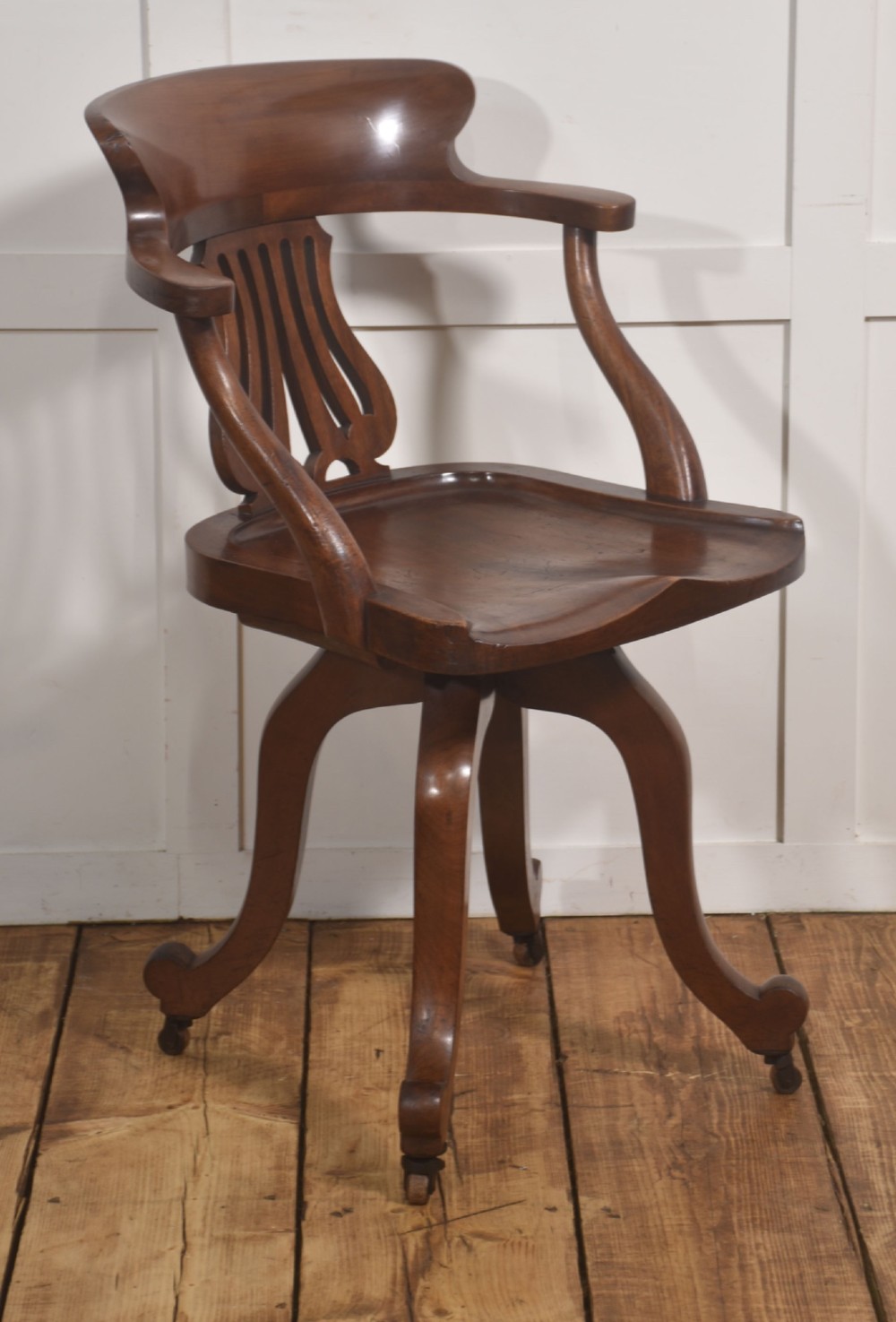 An antique mahogany revolving desk chair featuring a curved backrest, carved splat, shaped seat, and four splayed legs fitted with castors.