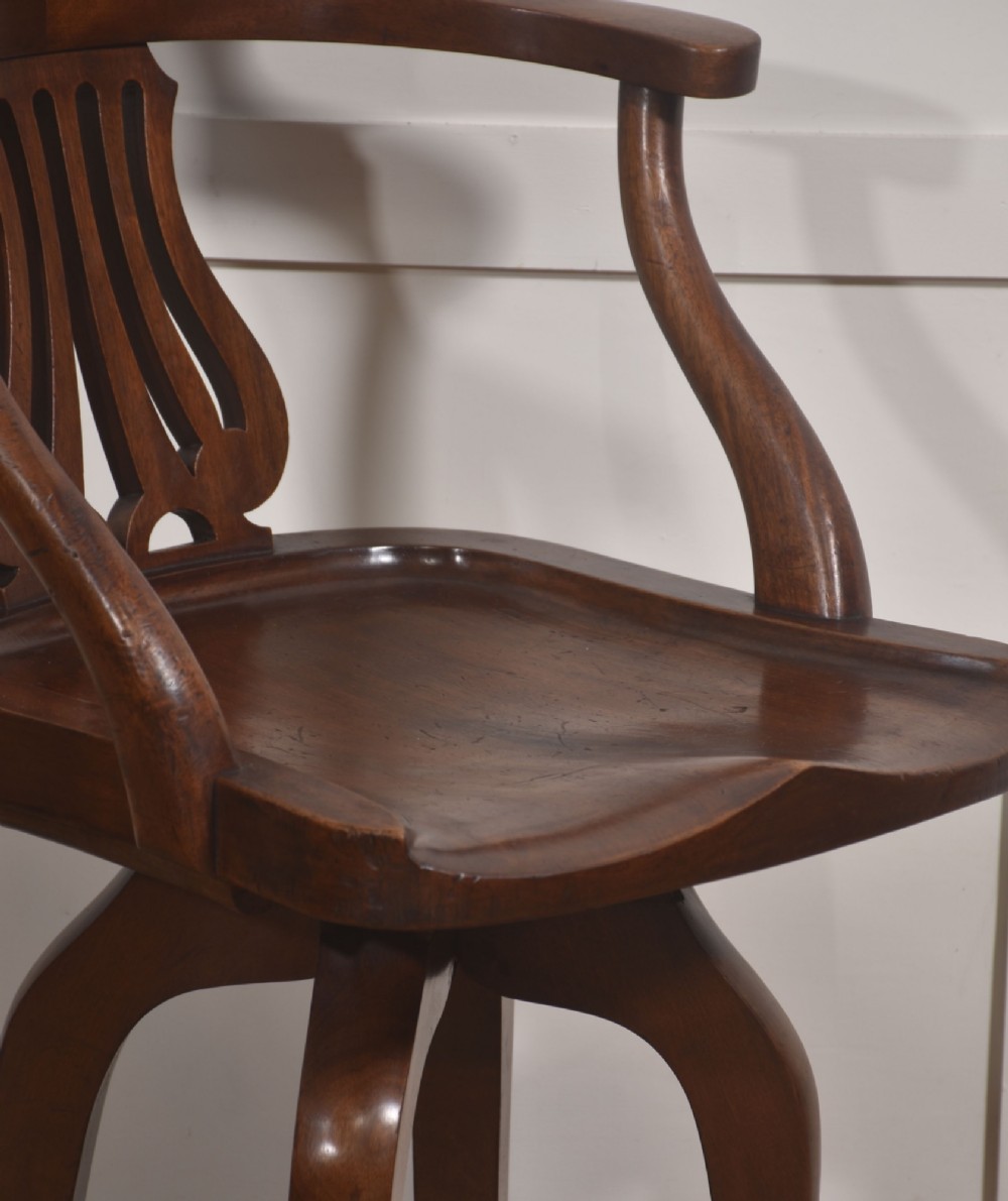 An antique mahogany revolving desk chair featuring a curved backrest, carved splat, shaped seat, and four splayed legs fitted with castors. View III
