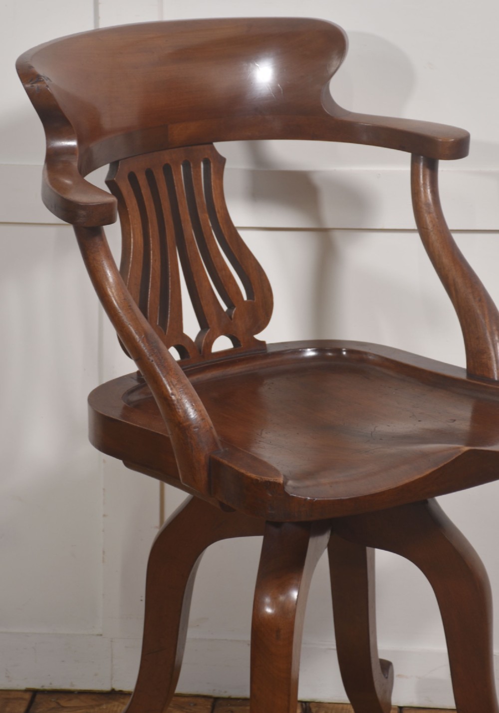 An antique mahogany revolving desk chair featuring a curved backrest, carved splat, shaped seat, and four splayed legs fitted with castors. View IV