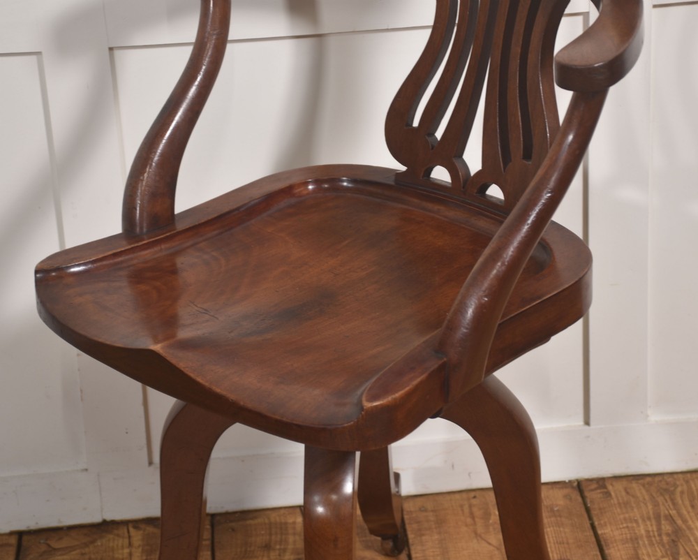An antique mahogany revolving desk chair featuring a curved backrest, carved splat, shaped seat, and four splayed legs fitted with castors. View VI