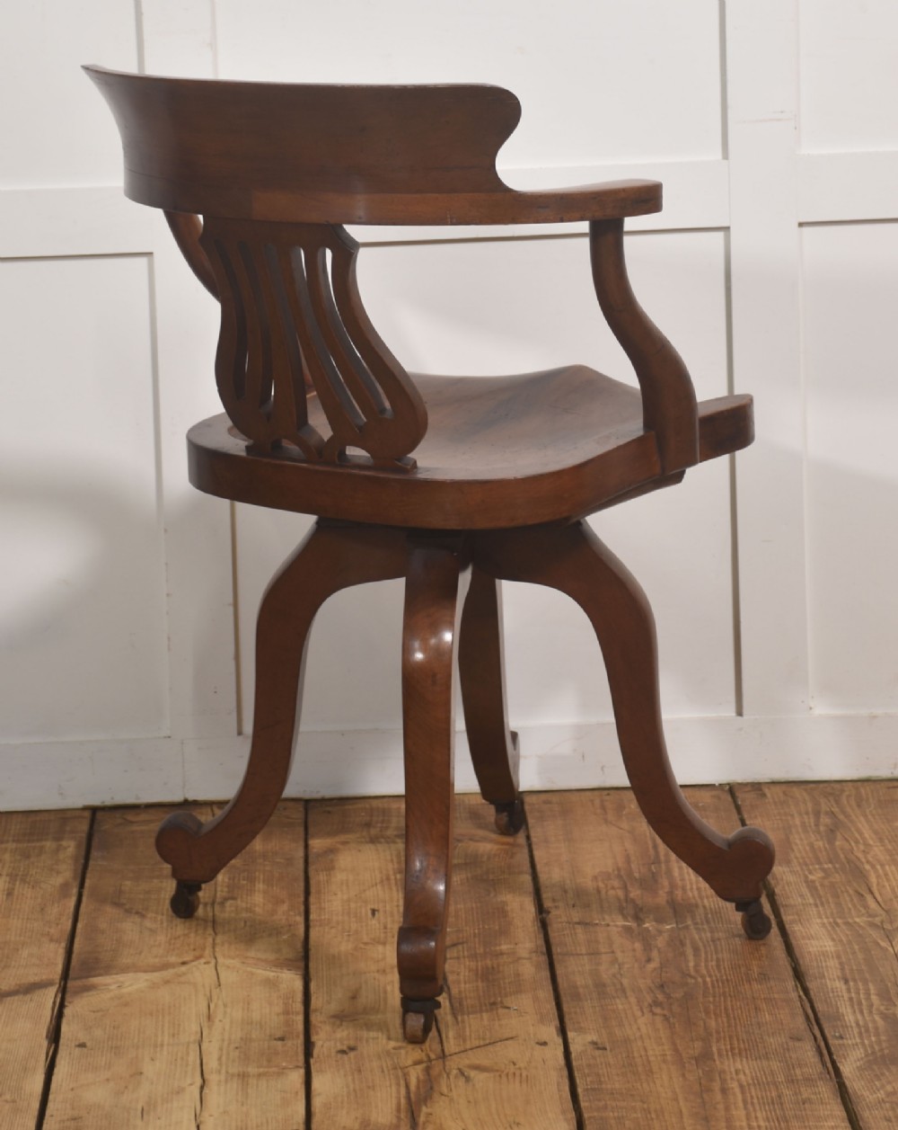 An antique mahogany revolving desk chair featuring a curved backrest, carved splat, shaped seat, and four splayed legs fitted with castors. View VII