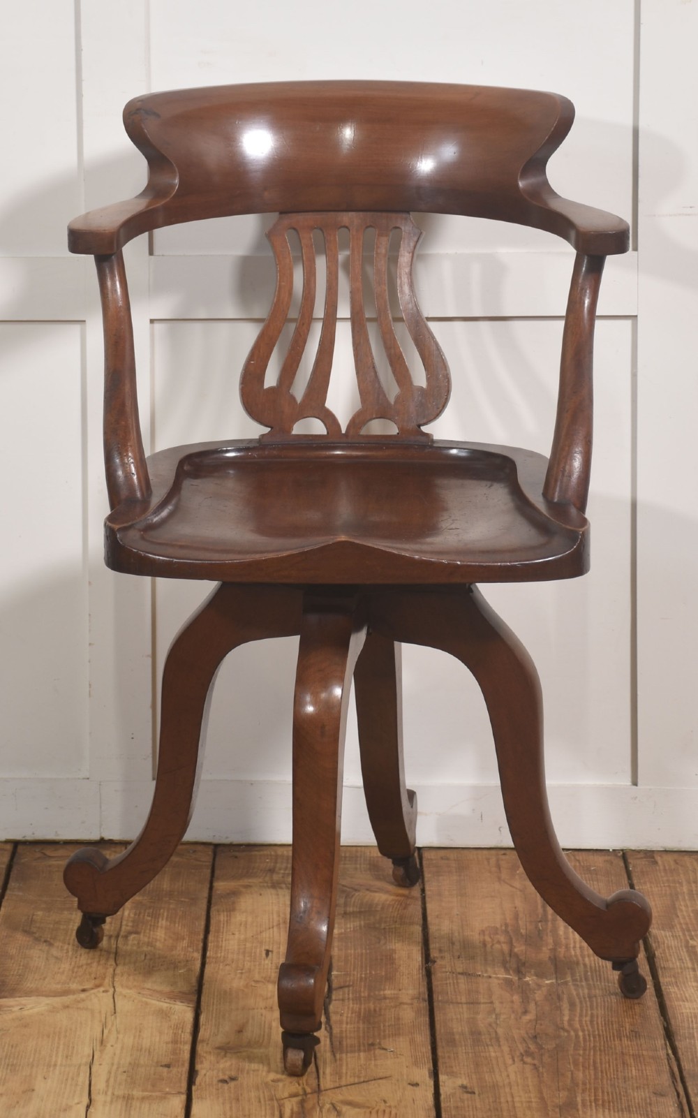 An antique mahogany revolving desk chair featuring a curved backrest, carved splat, shaped seat, and four splayed legs fitted with castors. View VIII