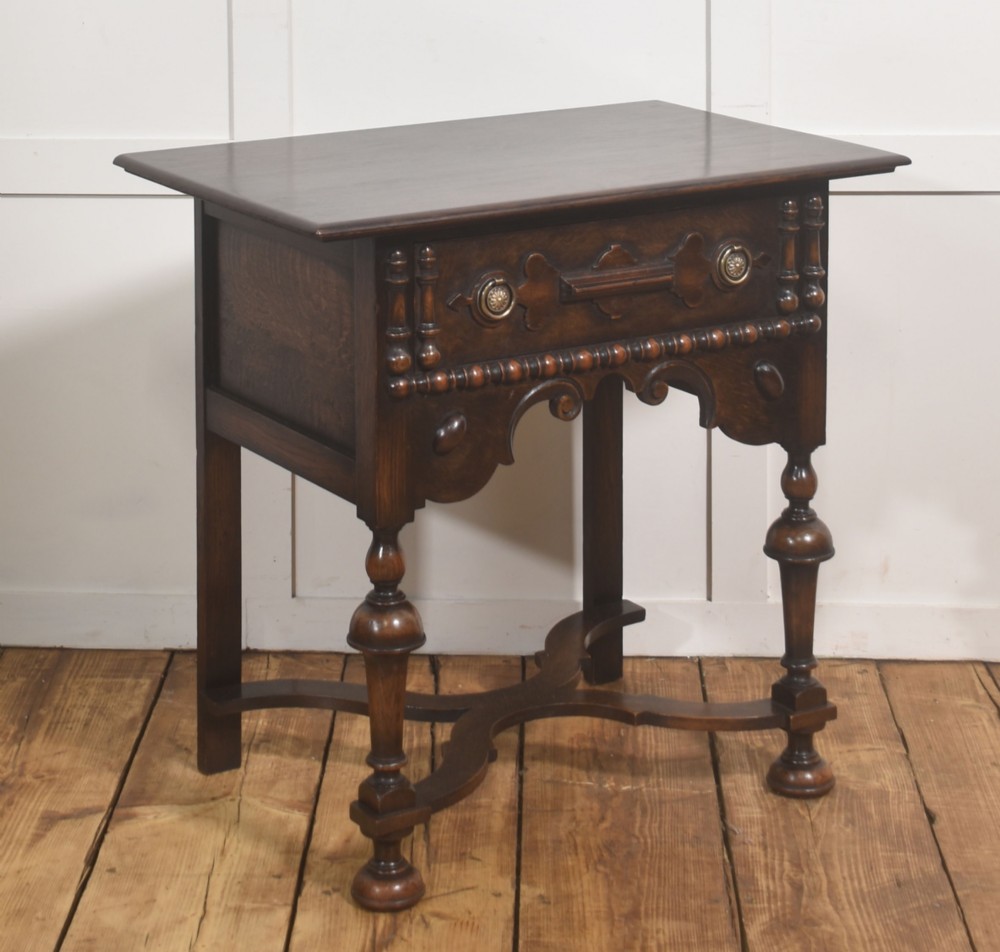 A dark brown oak side table featuring a single carved drawer with brass handles, a decorative apron, turned baluster legs, and a shaped cross stretcher. View III