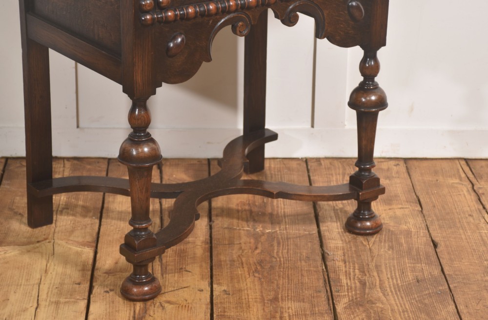 A dark brown oak side table featuring a single carved drawer with brass handles, a decorative apron, turned baluster legs, and a shaped cross stretcher. View IV