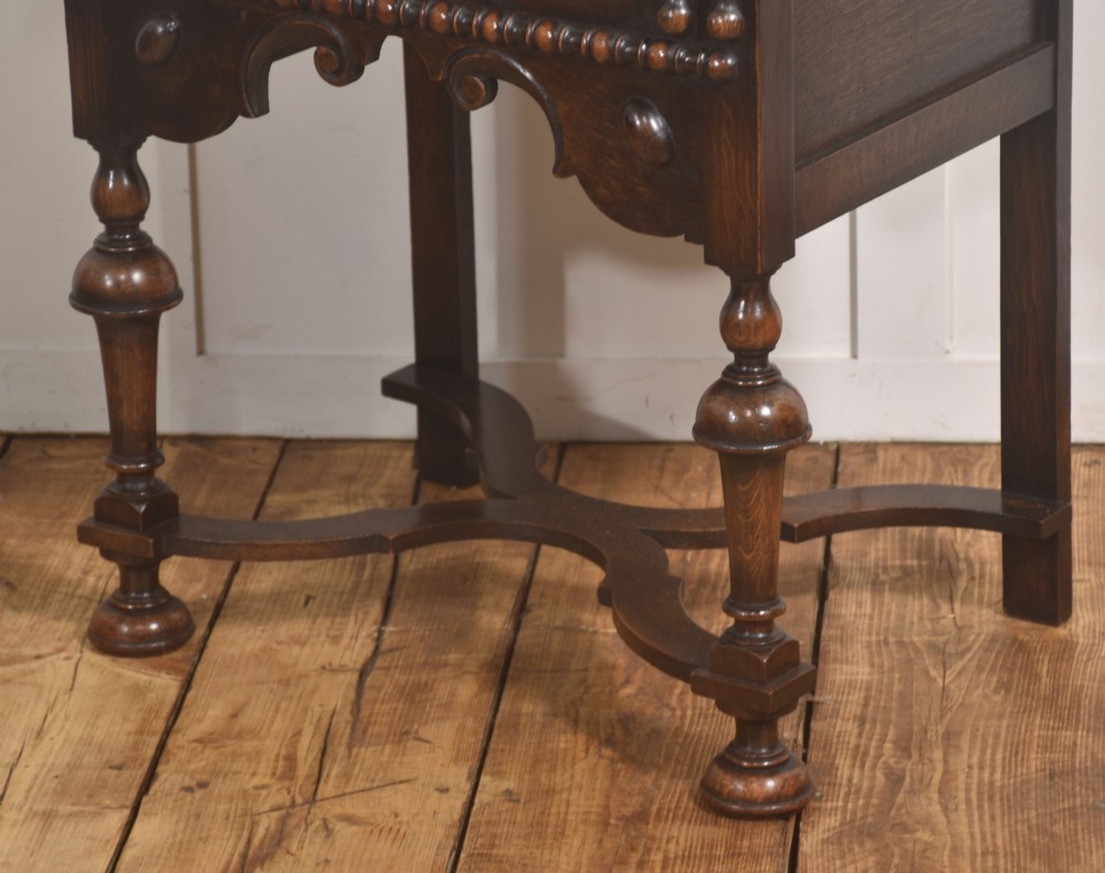 A dark brown oak side table featuring a single carved drawer with brass handles, a decorative apron, turned baluster legs, and a shaped cross stretcher. View VII