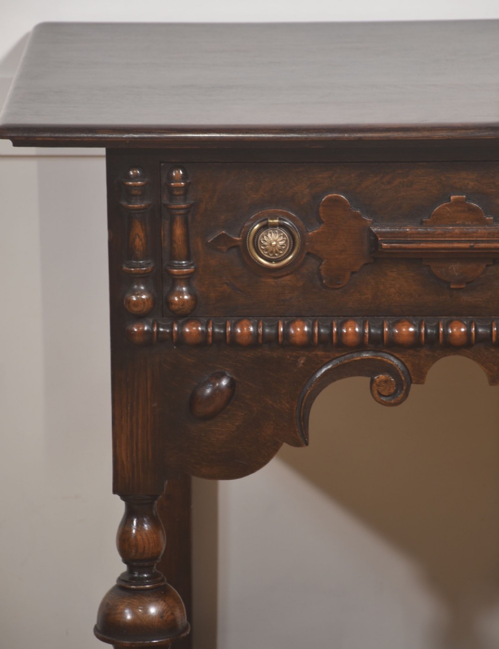 A dark brown oak side table featuring a single carved drawer with brass handles, a decorative apron, turned baluster legs, and a shaped cross stretcher. View VIII