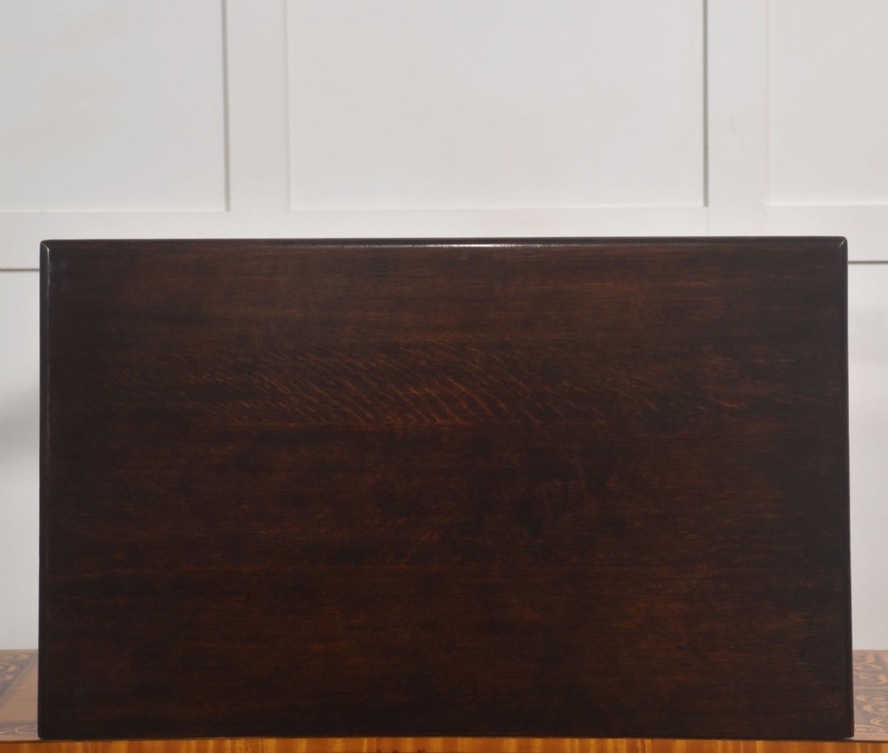 A dark brown oak side table featuring a single carved drawer with brass handles, a decorative apron, turned baluster legs, and a shaped cross stretcher. View X