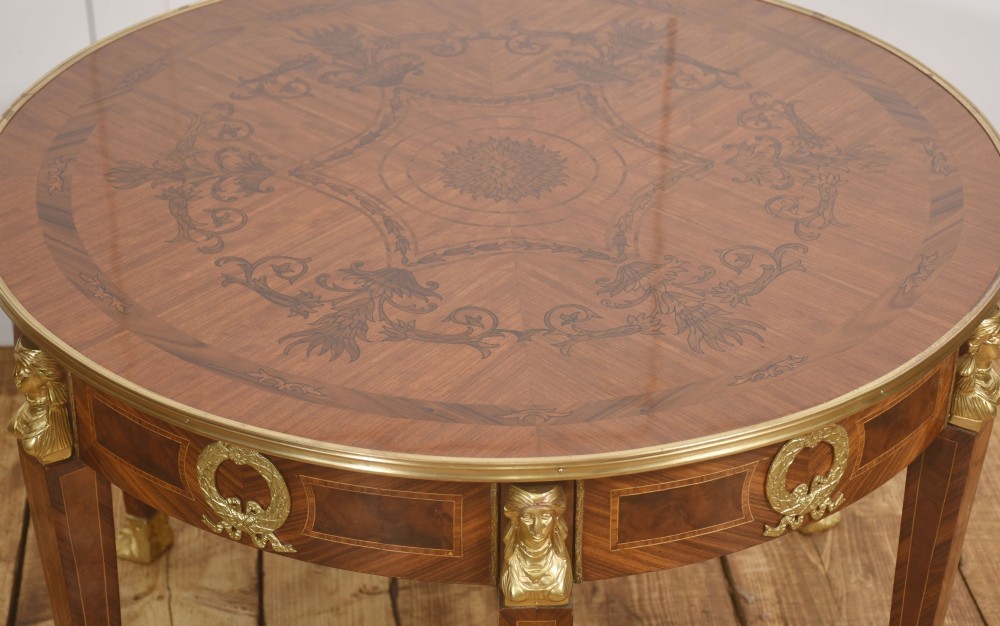 A round Louis XVI style coffee table featuring wood marquetry, warm brown veneers, tapered square legs, and decorative gilt brass female bust mounts. View IV