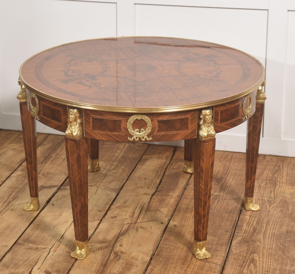A round Louis XVI style coffee table featuring wood marquetry, warm brown veneers, tapered square legs, and decorative gilt brass female bust mounts. View VII