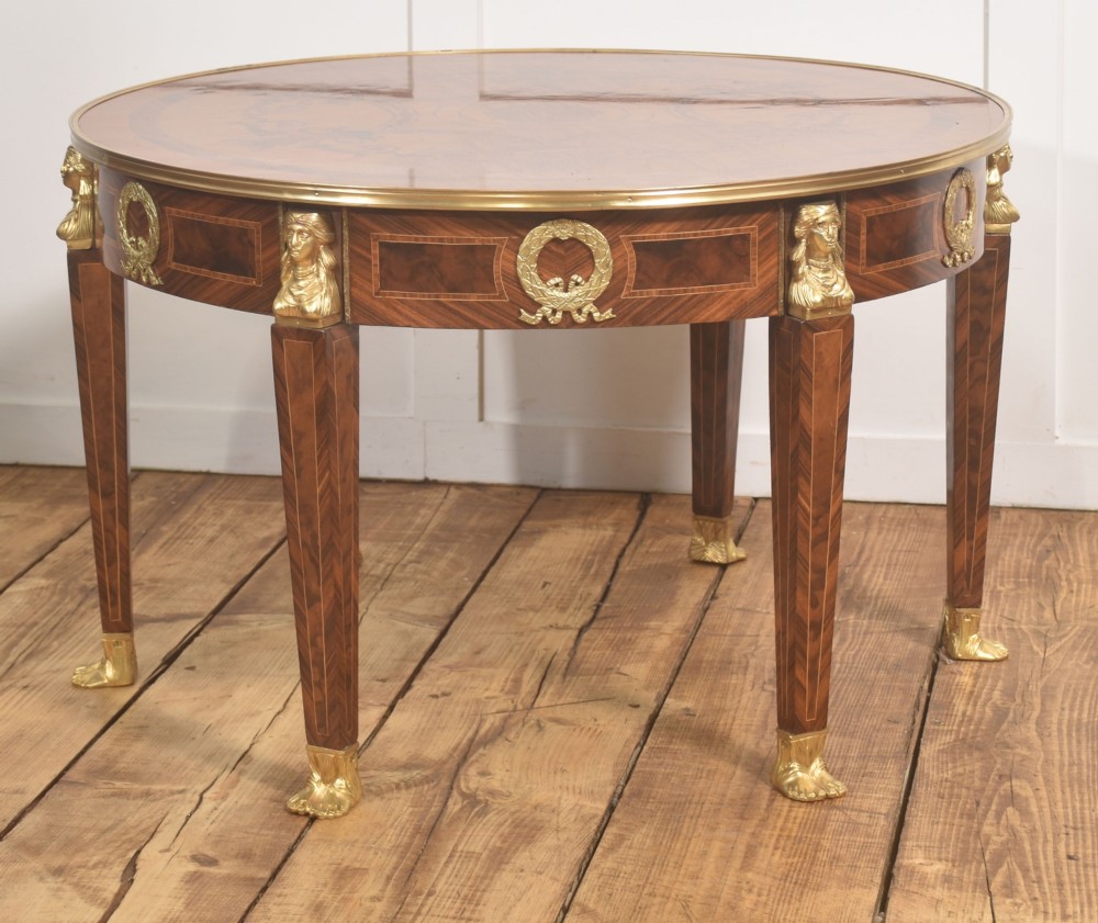 A round Louis XVI style coffee table featuring wood marquetry, warm brown veneers, tapered square legs, and decorative gilt brass female bust mounts. View VIII