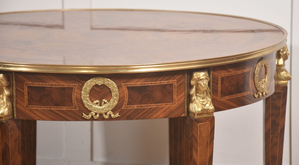A round Louis XVI style coffee table featuring wood marquetry, warm brown veneers, tapered square legs, and decorative gilt brass female bust mounts. View IX