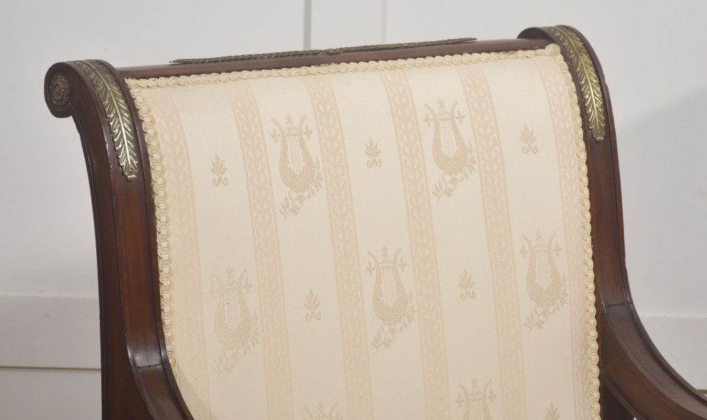 An Empire style mahogany armchair featuring cream upholstered silk fabric with lyre motifs, winged sphinx arm supports, and gilt brass winged lion front legs. View III