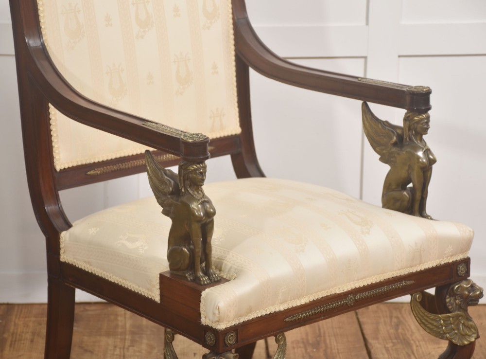 An Empire style mahogany armchair featuring cream upholstered silk fabric with lyre motifs, winged sphinx arm supports, and gilt brass winged lion front legs. View IV