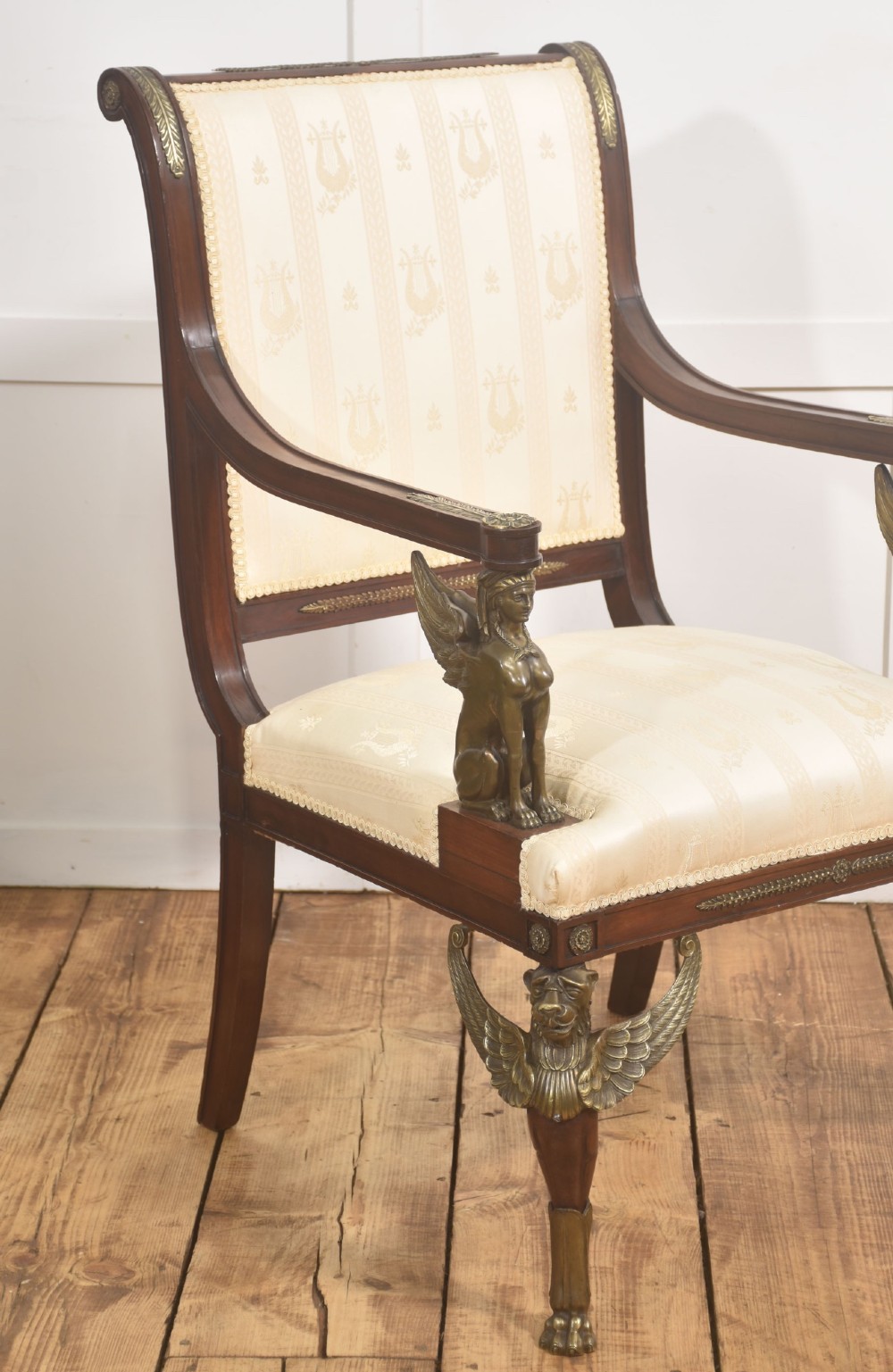 An Empire style mahogany armchair featuring cream upholstered silk fabric with lyre motifs, winged sphinx arm supports, and gilt brass winged lion front legs. View V