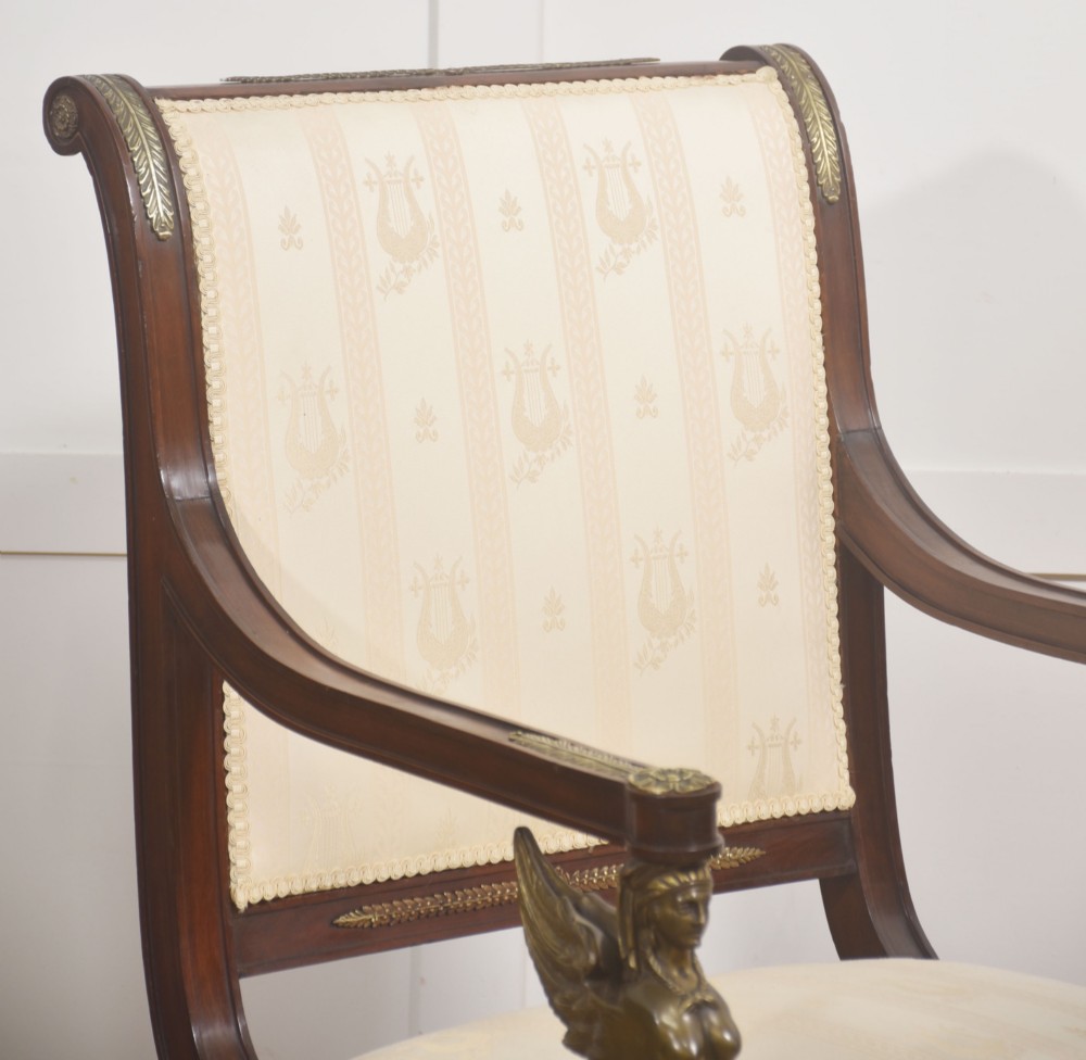 An Empire style mahogany armchair featuring cream upholstered silk fabric with lyre motifs, winged sphinx arm supports, and gilt brass winged lion front legs. View VI